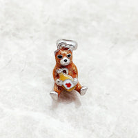 Brown bear charm holding a bottle.