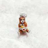 Brown bear charm holding a bottle.